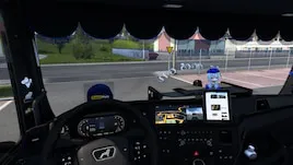 Vue intérieure d’une cabine de camion dans Euro Truck Simulator 2 avec tableau de bord, volant, GPS et pare-brise donnant sur une zone de stationnement.